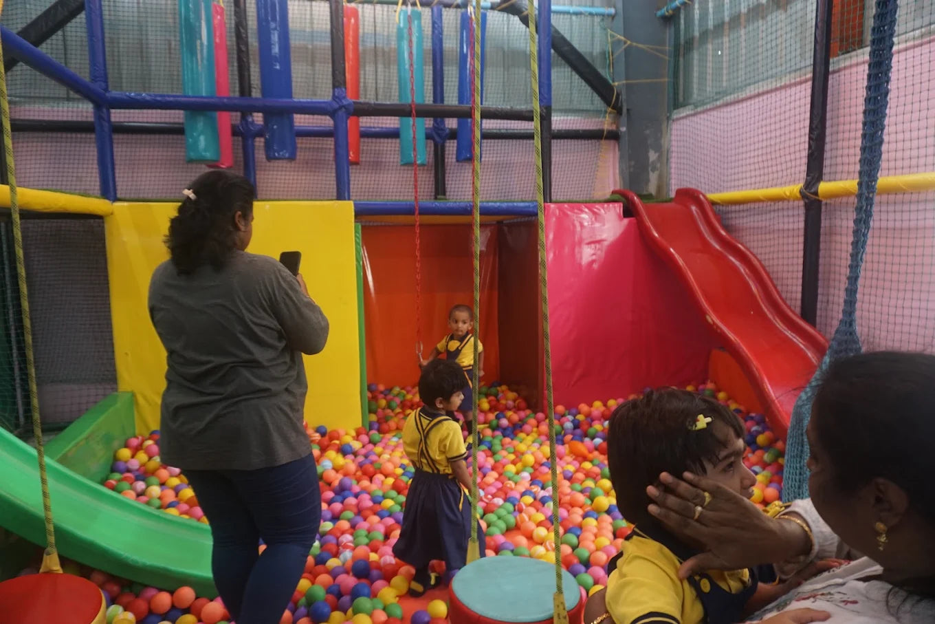 Children play in a ball pit with a slide, while an adult takes a photo.