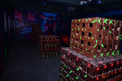 Dark room with stacks of wooden crates illuminated by colorful lights for playing laser tag