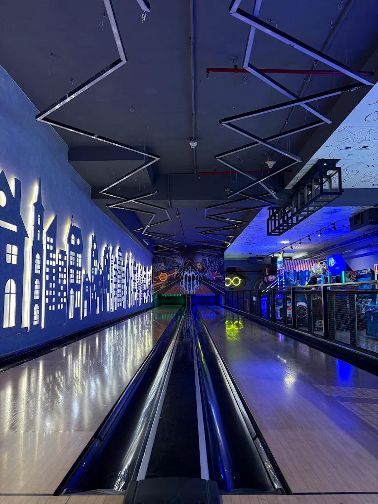 Bowling alley with neon lights and a cityscape mural on the wall.
