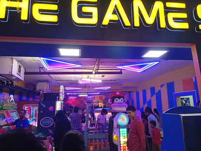 An arcade with neon lights and various game machines, filled with people of all ages playing and watching.