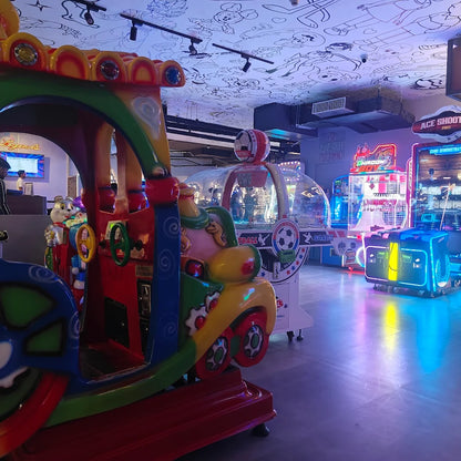 A colorful children's train ride in an arcade with various game machines.
