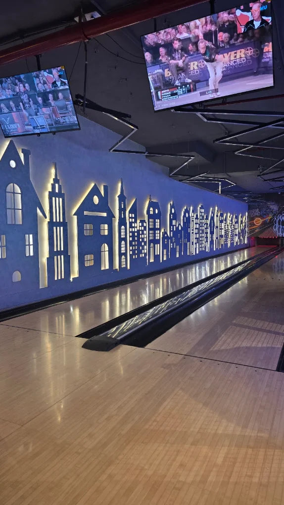 A bowling alley with a cityscape mural on the wall and screens showing a sports game.