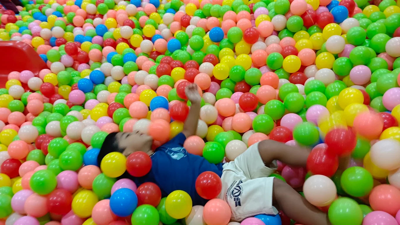 A young child plays in a ball pit filled with colorful balls.
