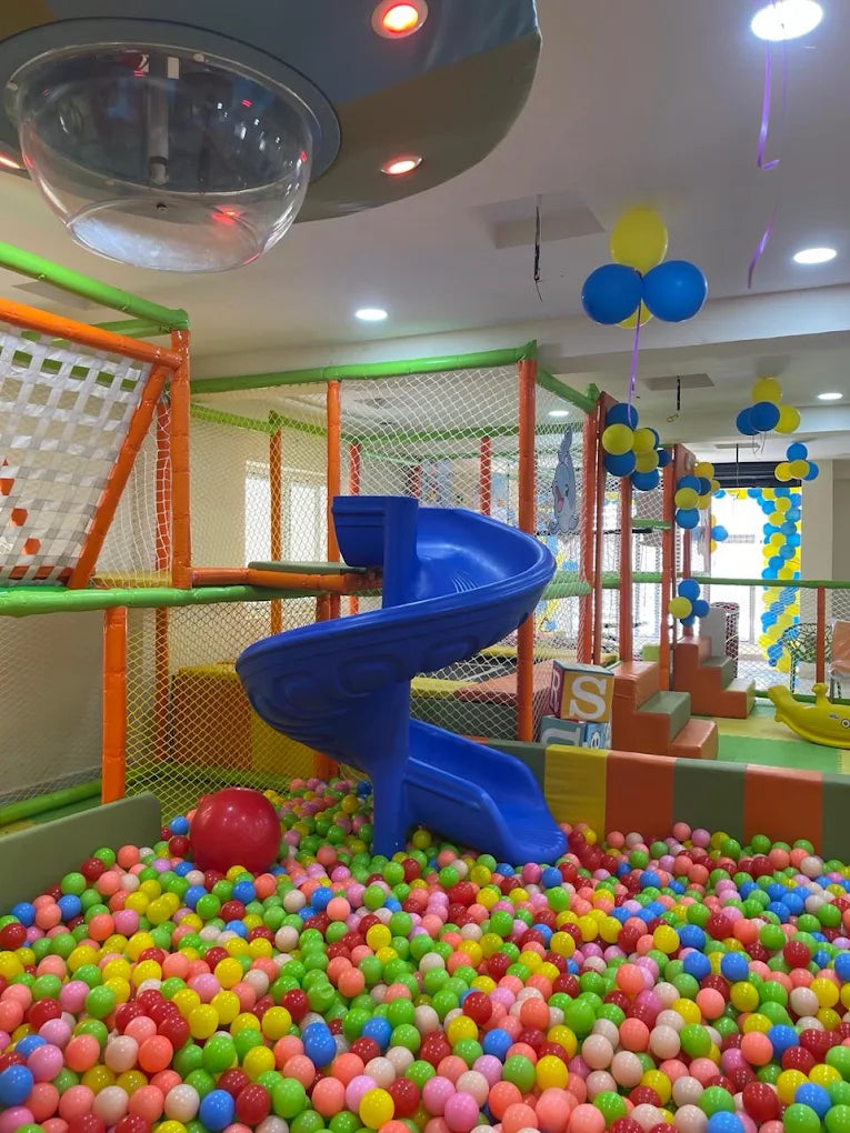 A colorful ball pit with a blue slide in a children's play area.