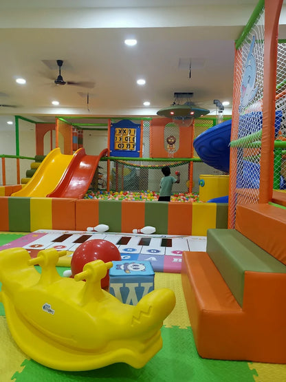 A child plays in a colorful indoor playground with slides, a ball pit, and a large yellow rocking toy.