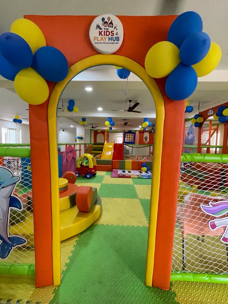 A colorful indoor play area for children, decorated with balloons, featuring slides, ball pits, and play structures.