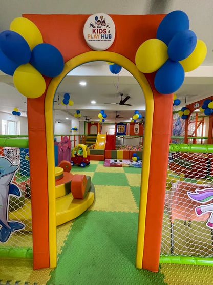 A colorful indoor play area for children, decorated with balloons, featuring slides, ball pits, and play structures.