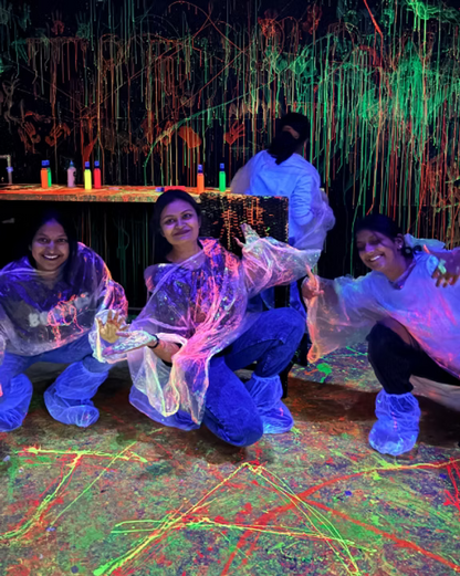 Young adults in a neon-lit room, splattered with paint, wearing protective gear.
