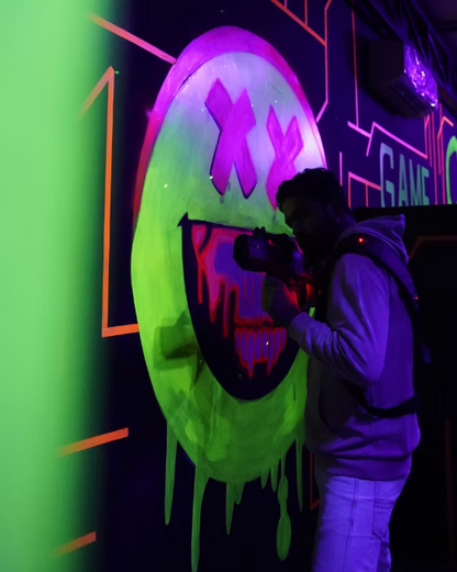 A person plays laser tag in a neon-lit arena with a large, glowing smiley face mural.