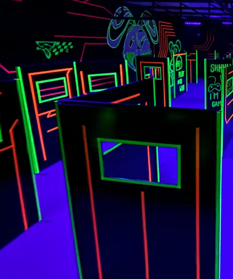 A neon-lit laser tag arena with glowing orange and green lines on black walls.
