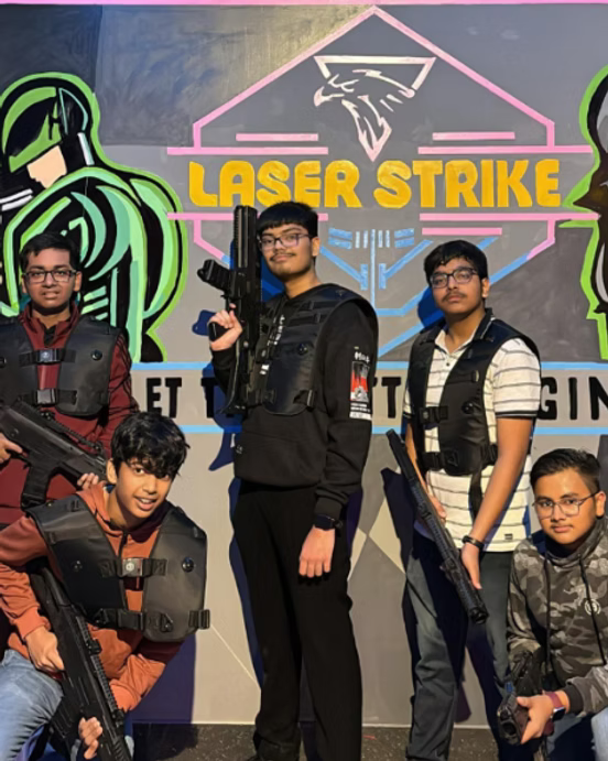 Five young people in laser tag vests and holding phasers pose in front of a "Laser Strike" mural.