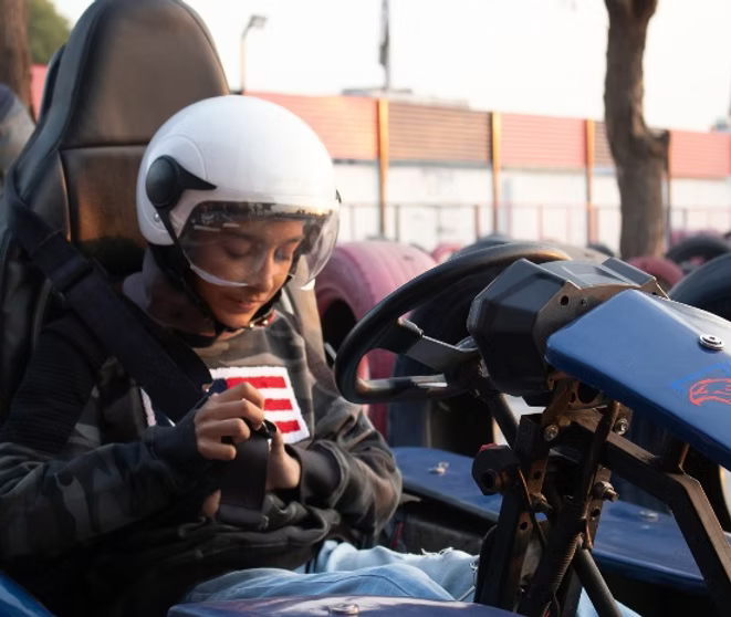 A young person in a helmet fastens their seatbelt in a go-kart.