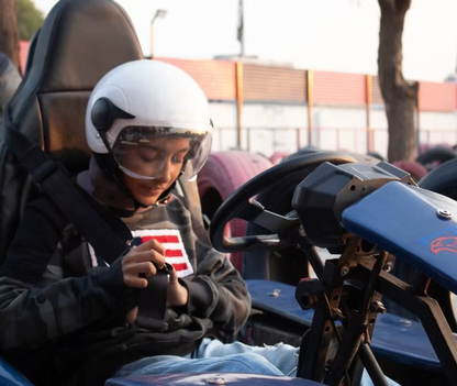 A young person in a helmet fastens their seatbelt in a go-kart.