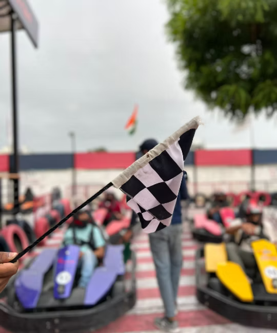 A checkered flag waves at a go-kart race with young adults in the background.