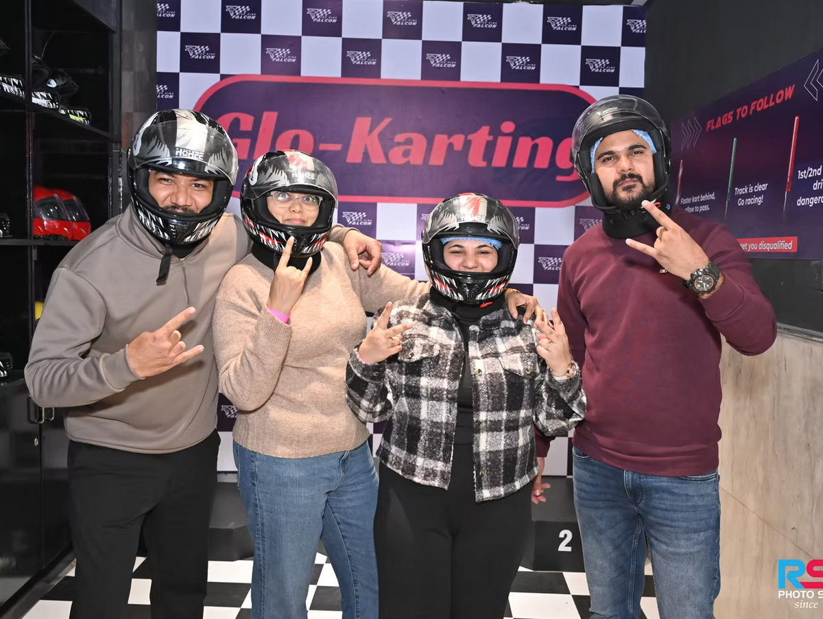 Two couples in go-karting helmets pose for a photo at an indoor track.