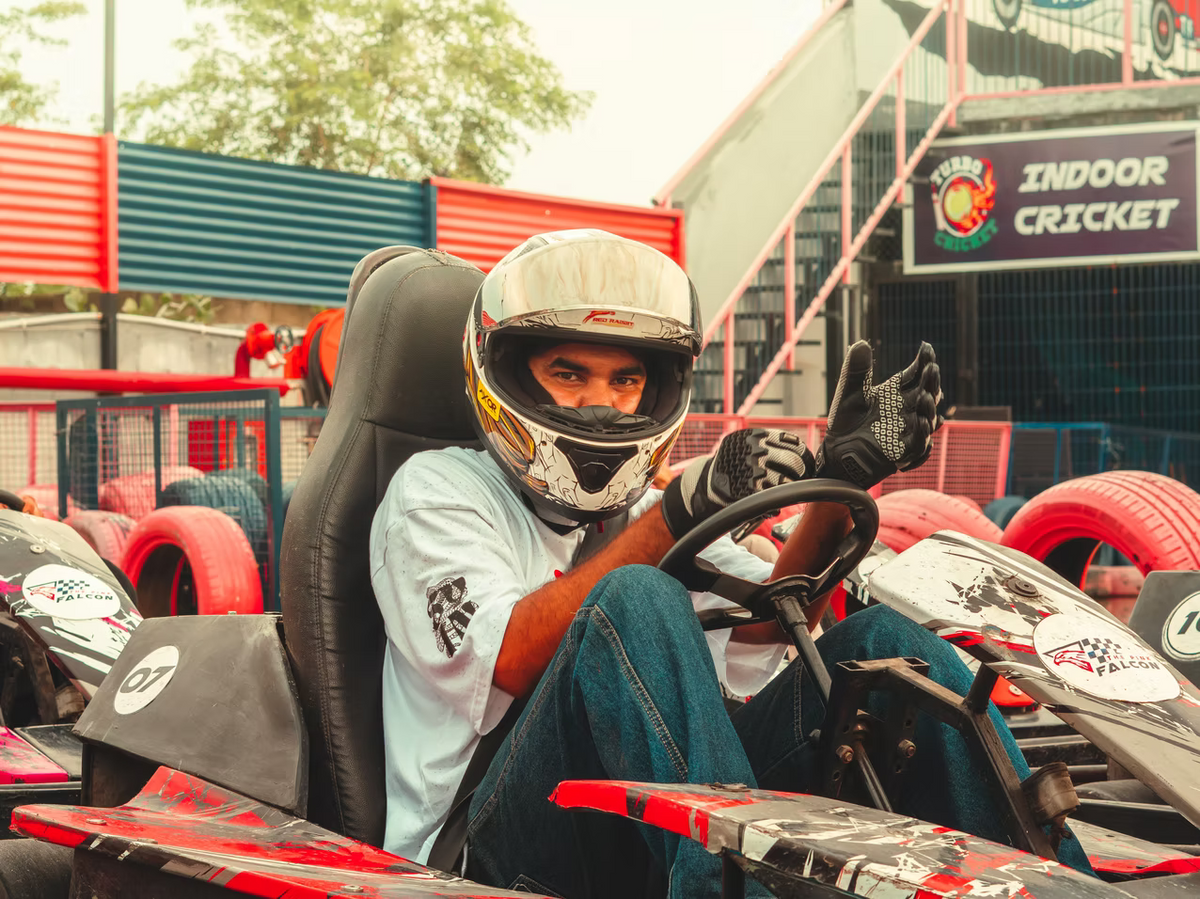 A young man in a go-kart helmet gives a thumbs up while sitting in a go-kart.