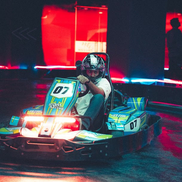 Person driving a go-kart on a track with red and blue lights in the background