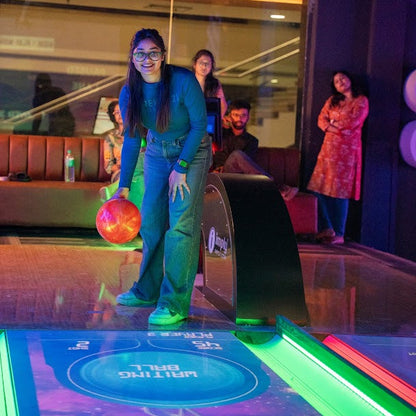 Woman in a bowling alley with a ball and pins, surrounded by other people.