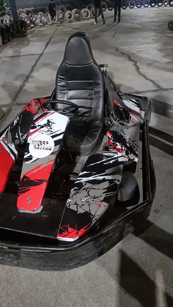 A go-kart with a black leather seat and a red, white, and black splatter design sits on a concrete track.