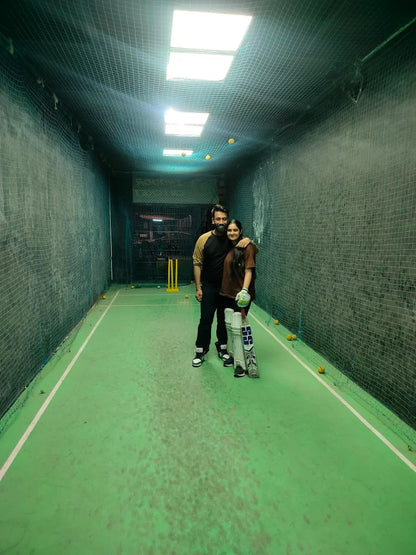 A young couple stands in a cricket net with bats and balls.