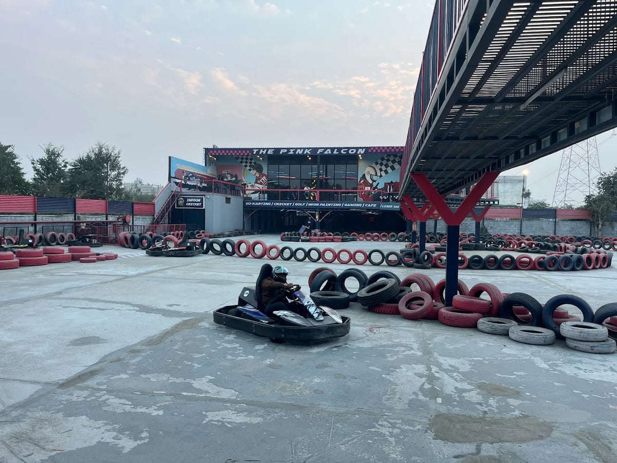 Go-karting track with people racing go-karts in front of "The Pink Falcon" building.