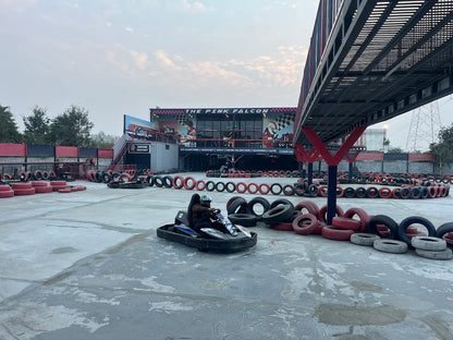 Go-karting track with people racing go-karts in front of "The Pink Falcon" building.