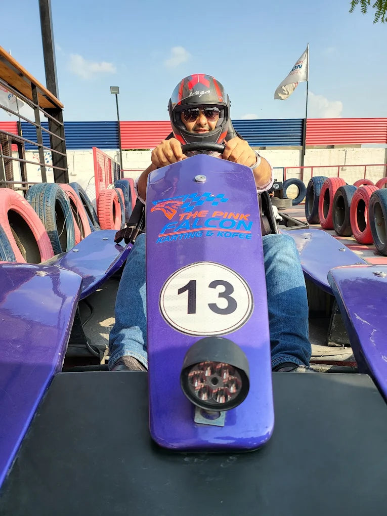 A person in a helmet drives a purple go-kart with the number 13 on it at an outdoor track.