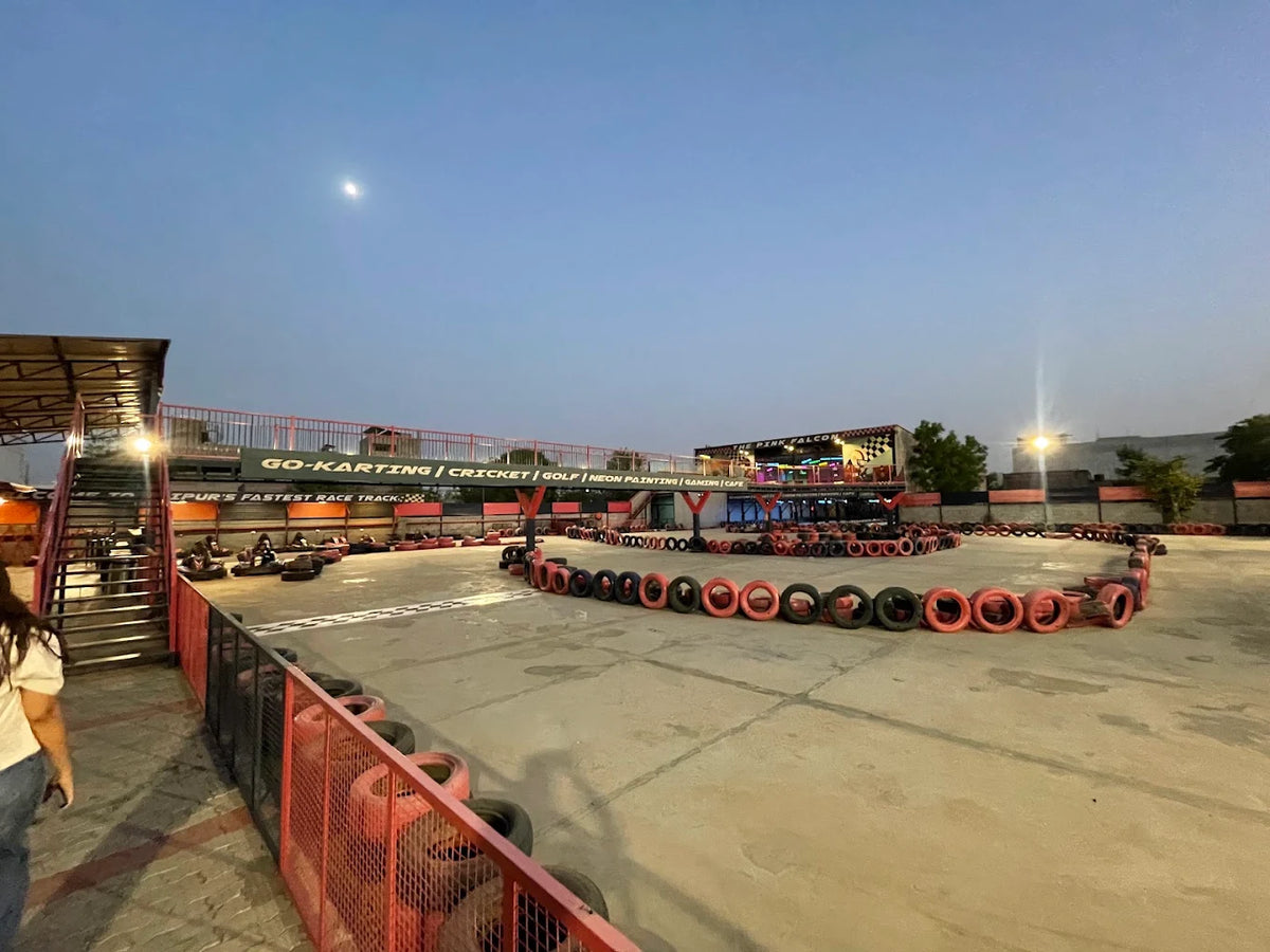 An outdoor go-kart track with tire barriers and a building in the background.