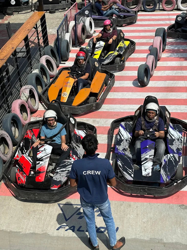 Adults in go-karts at an outdoor track, with a crew member observing.