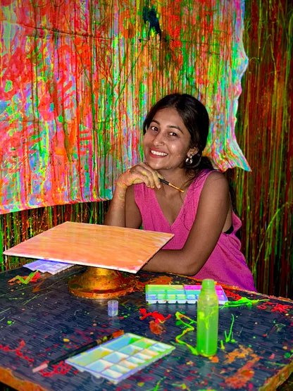 A young woman smiles while painting in a colorful, paint-splattered studio.