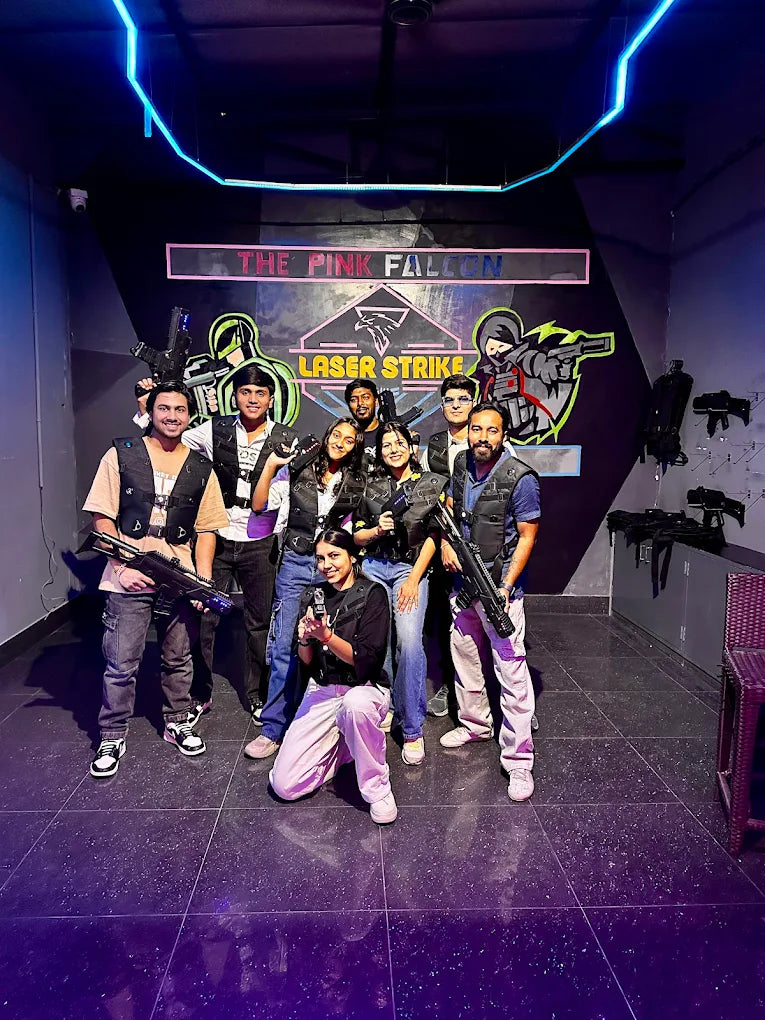 A group of young adults poses with laser tag guns in a dimly lit arena. They are wearing vests and ready for a game.