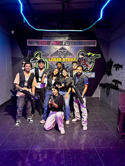 A group of young adults poses with laser tag guns in a dimly lit arena. They are wearing vests and ready for a game.