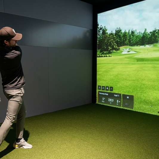 A man practices golf in a simulator room, with a virtual golf course displayed on a large screen.