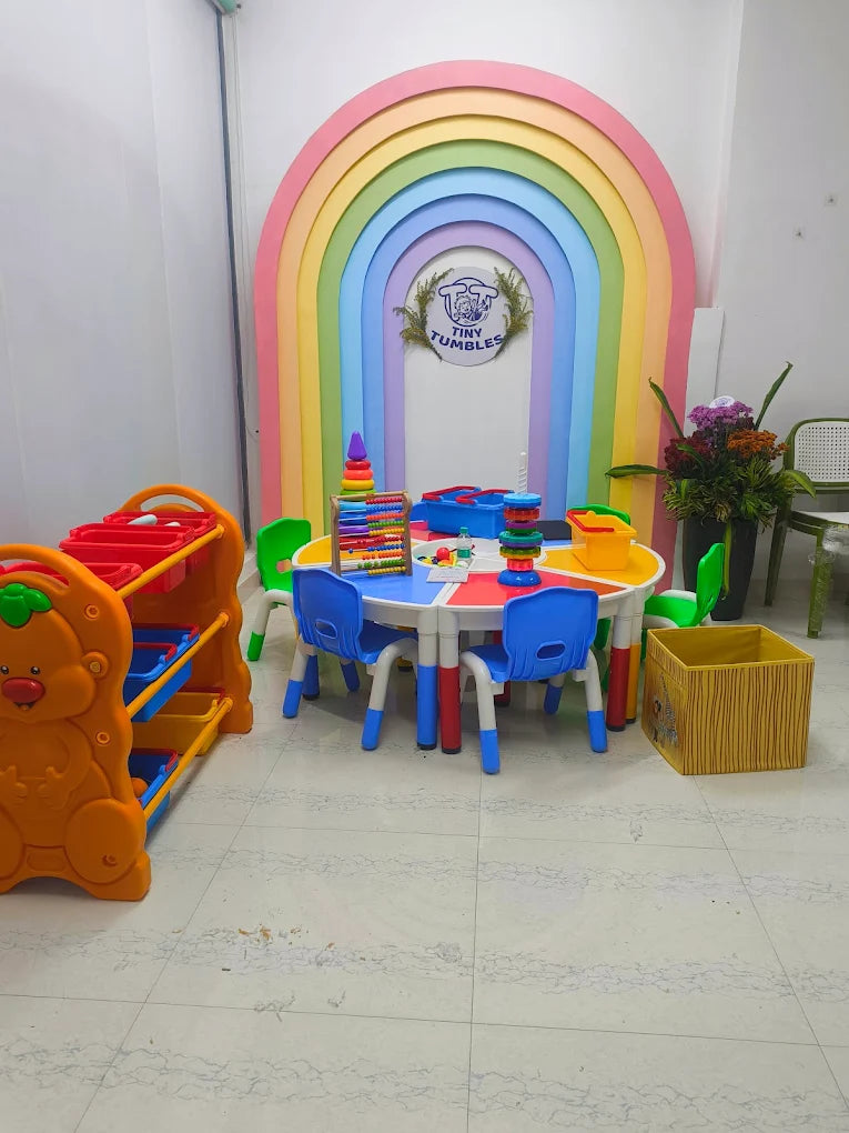 A colorful children's play area with a rainbow arch, small tables, chairs, and toys.