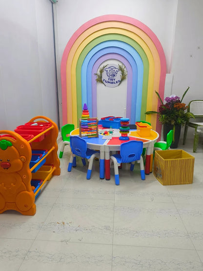 A colorful children's play area with a rainbow arch, small tables, chairs, and toys.