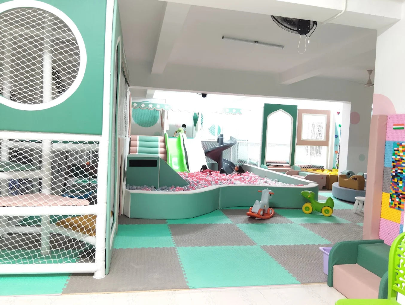 A colorful indoor playground with a ball pit, slides, and soft play structures for young children.