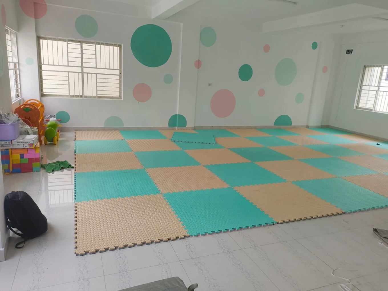 A brightly colored playroom with foam floor mats and wall decorations for young children.