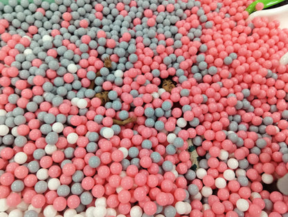 Children play in a ball pit filled with pink and gray balls.