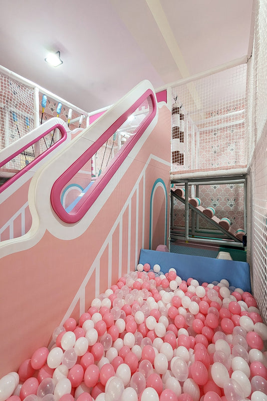 A pink and white indoor playground with a ball pit and slides for children.