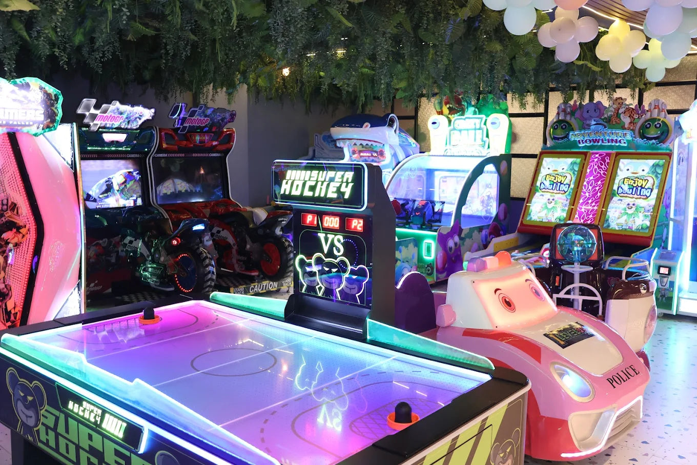 Indoor arcade featuring neon-lit air hockey table, car racing games, and colorful ticket redemption machines