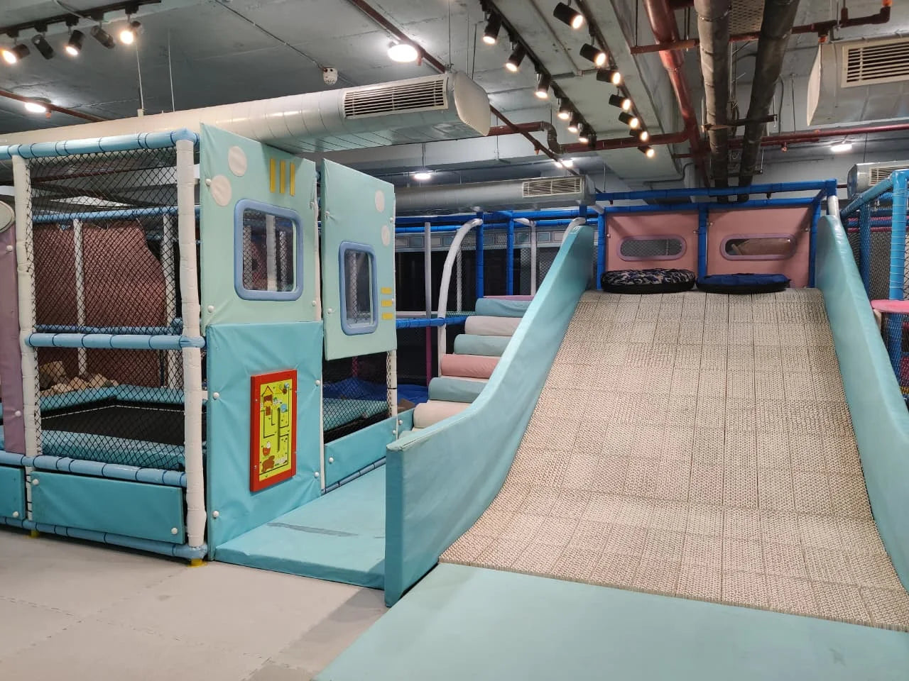 Indoor kids play area featuring soft climbing steps, padded slide, and enclosed safety play structures under warm lighting