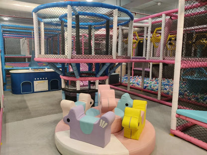 Indoor soft play area with pastel animal-shaped seats and multi-level climbing structures surrounded by safety netting