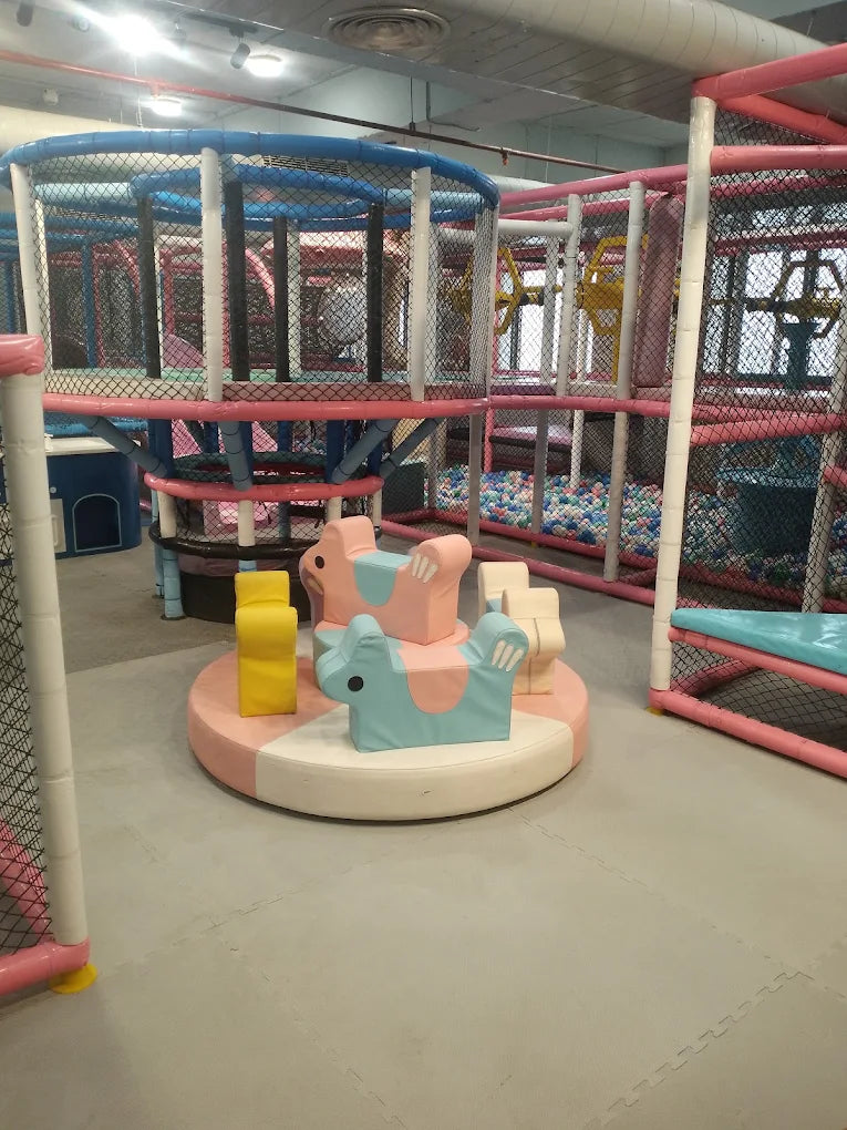Soft foam animal-shaped rides on a circular platform within a large indoor play structure with climbing nets and ball pit