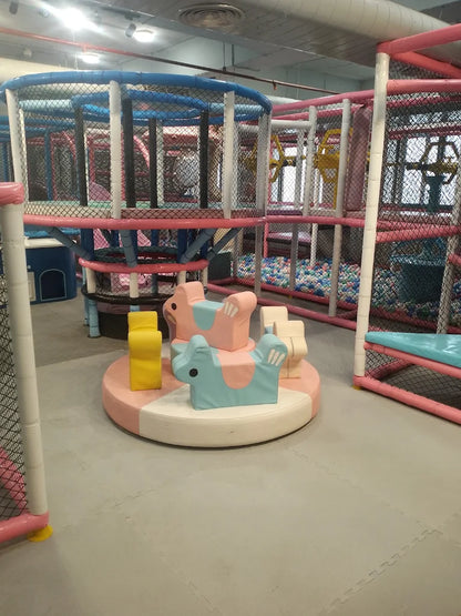 Soft foam animal-shaped rides on a circular platform within a large indoor play structure with climbing nets and ball pit