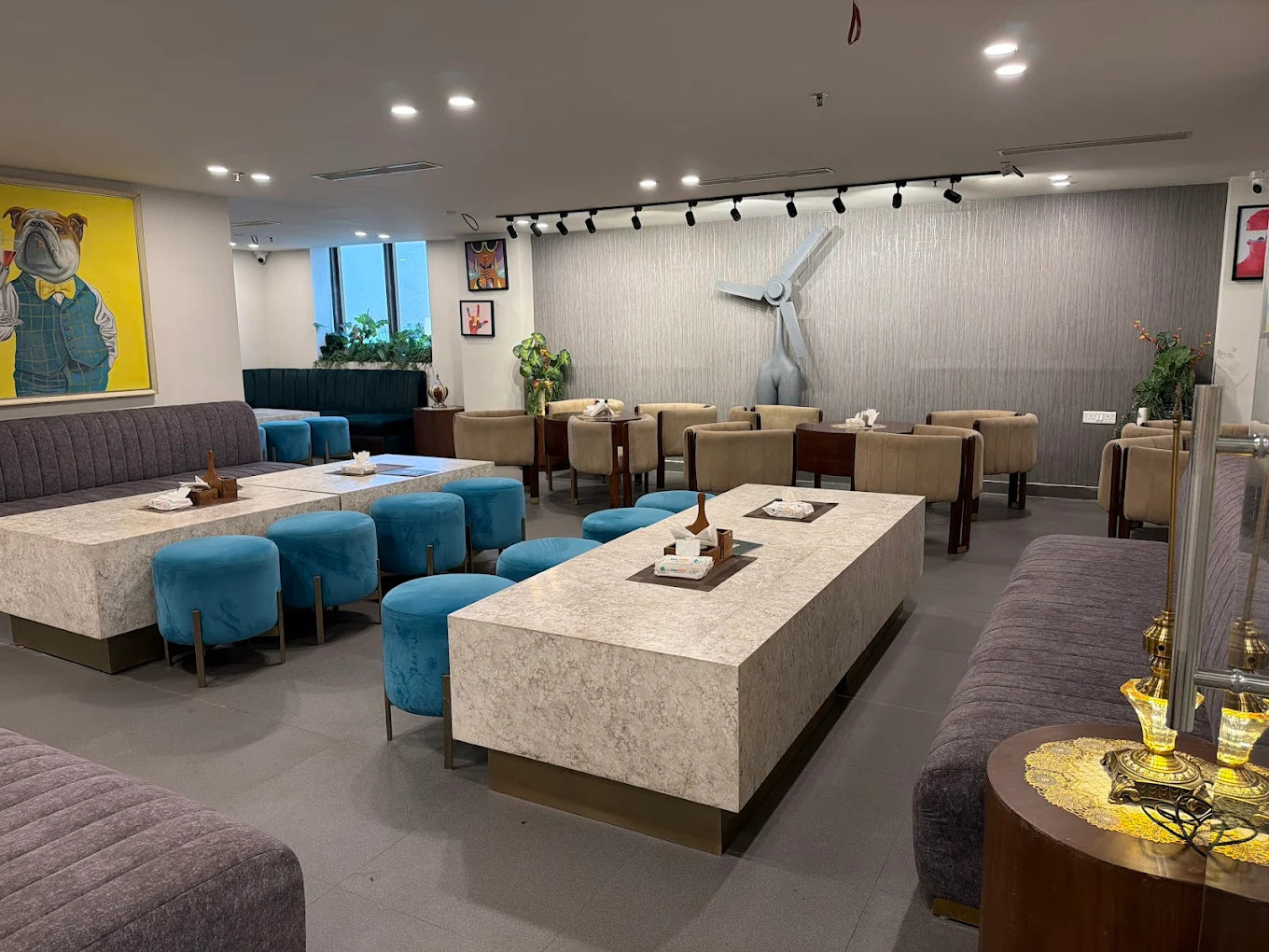 Contemporary indoor seating area with cushioned benches, blue stools, modern art, and ambient lighting in a play zone lounge