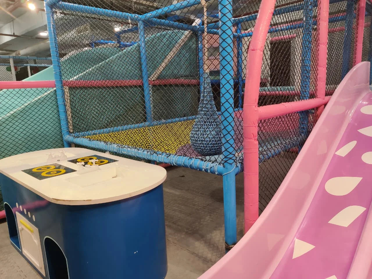 Indoor play structure with pastel pink slide, blue padded climbing frame, and netted enclosure for safe kids fun