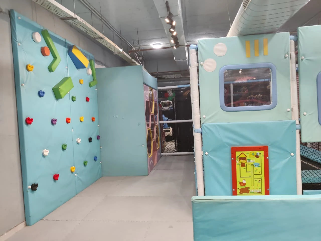Soft padded climbing wall and enclosed play structures with windows in a calm indoor play area for kids