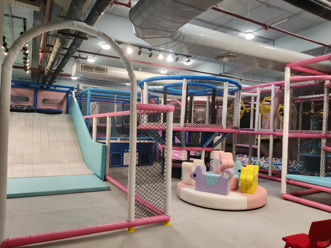 Indoor play area with soft climbing structures, padded ramps, and colorful animal ride units in a safe space