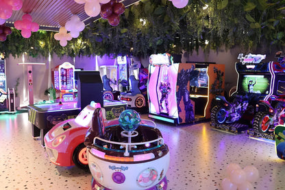 Vibrant indoor play zone with colorful arcade machines, interactive rides, and lush greenery overhead in a lively setting