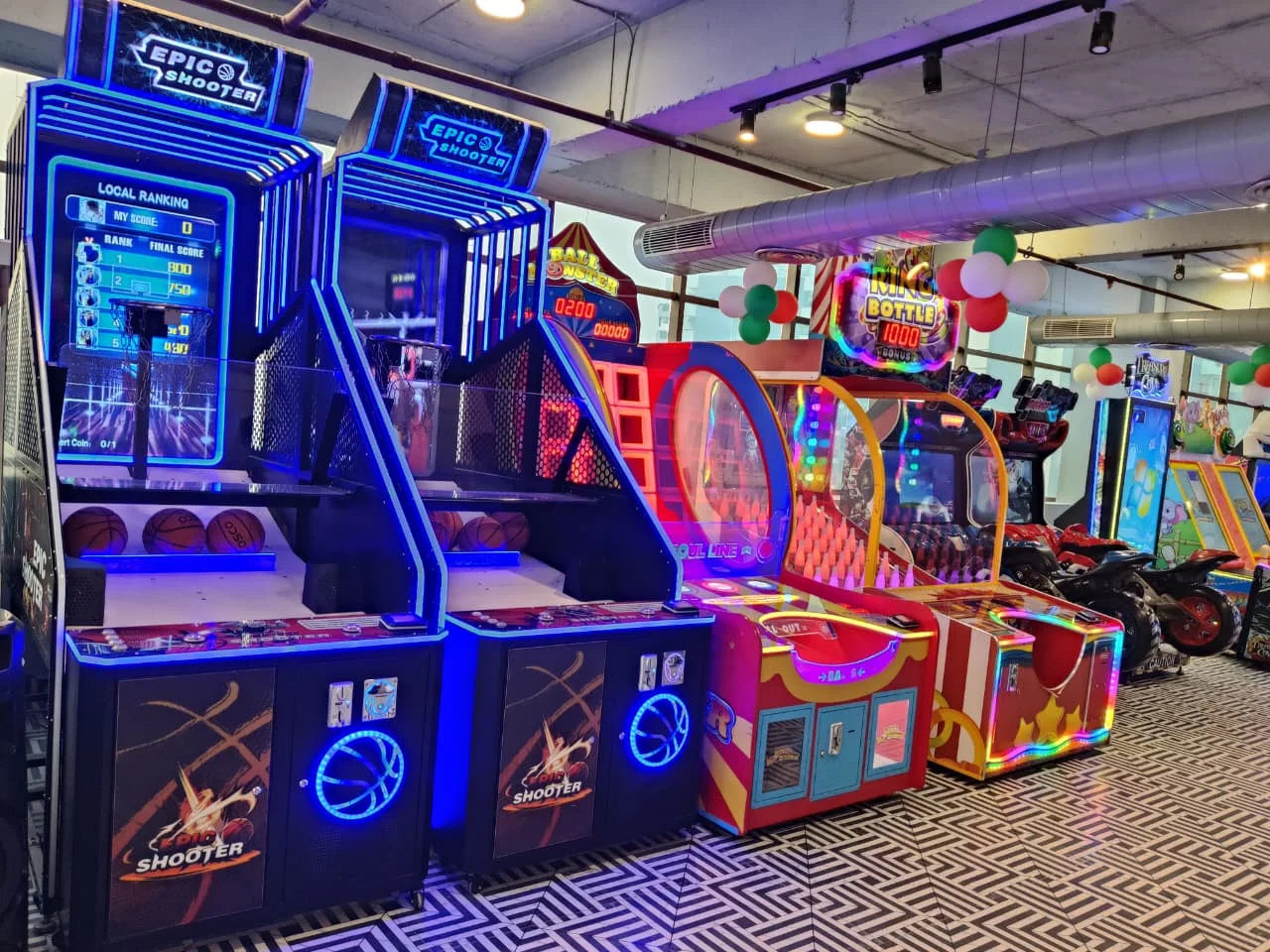 Brightly lit arcade featuring basketball shooting games, colorful ball toss machines, and racing simulators indoors
